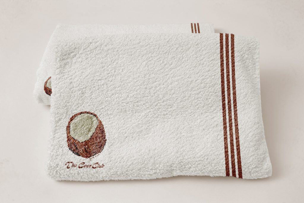 Soft white towel with brown stripes and logo, displayed on a neutral background.